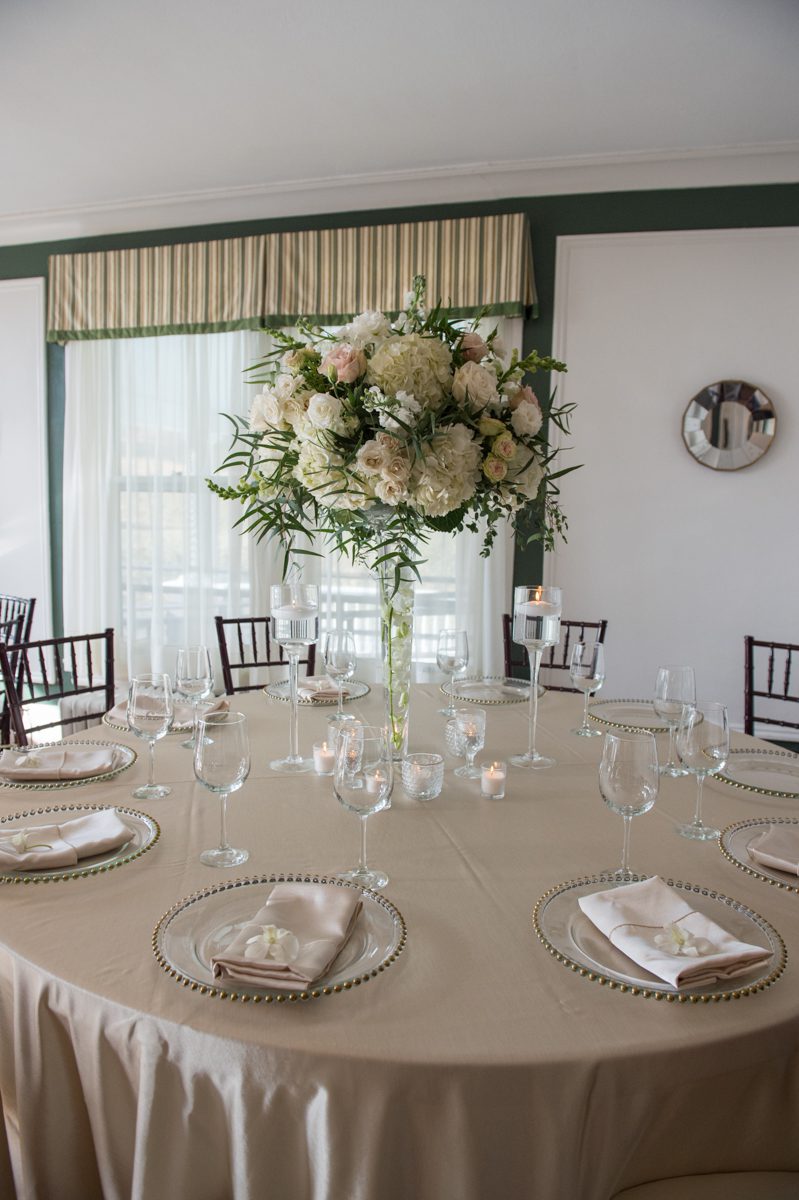 white floralarrangement in long stemmed vase on a table with biege linens