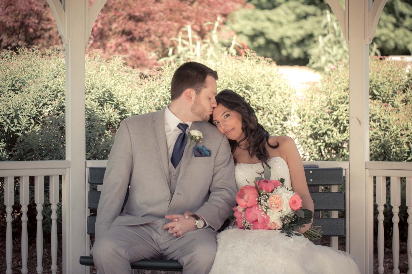 groom-kissing-bride-on-forehead-sitting-in-summer-gazebo