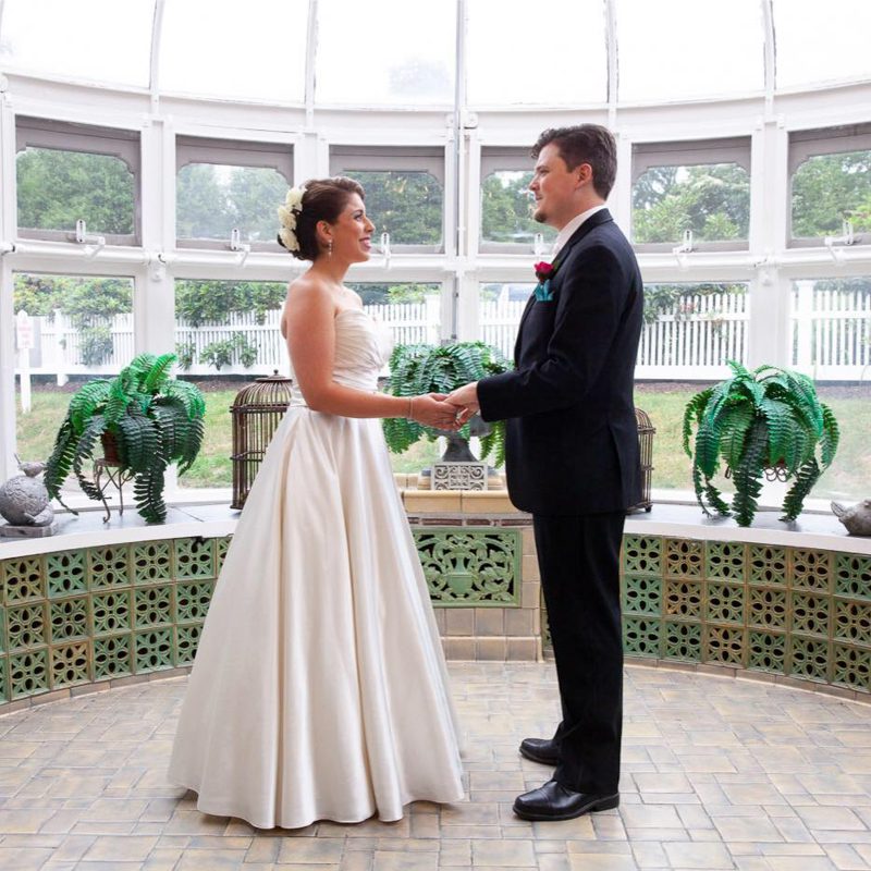 rachel-and-robert-holdiing-hands-in-glass-conservatory-cuban-theme-wedding